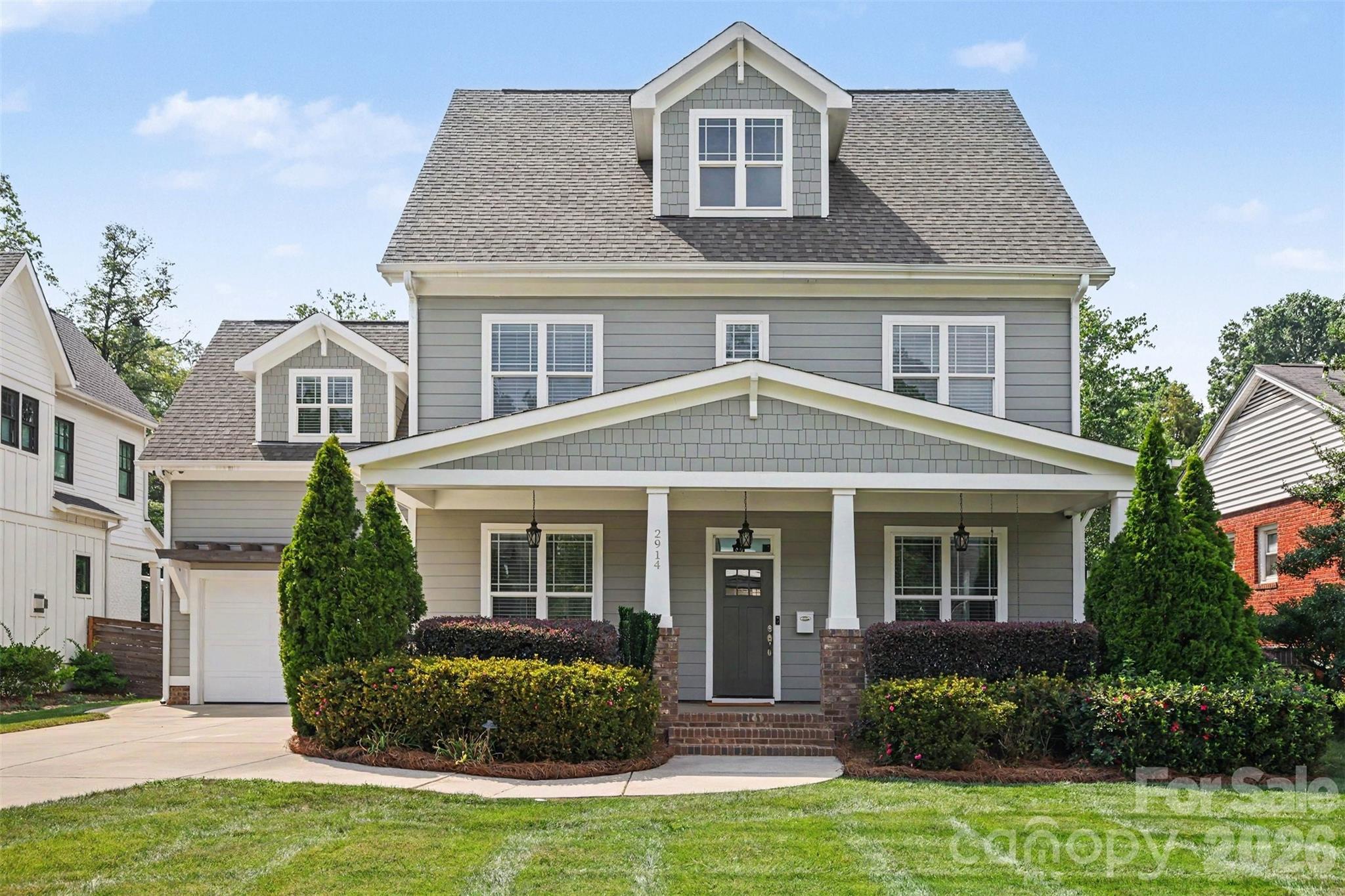 Gray two-story house with a covered porch, attached garage, dormers, and landscaped front yard.