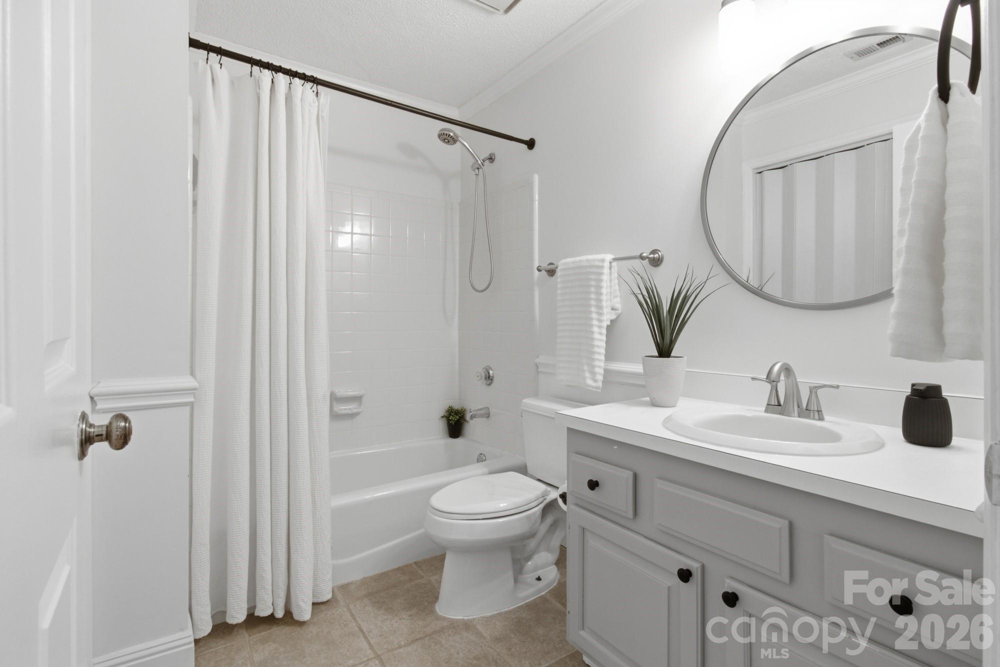 Bathroom with a white tub and shower curtain, toilet, and vanity beneath a large round mirror.