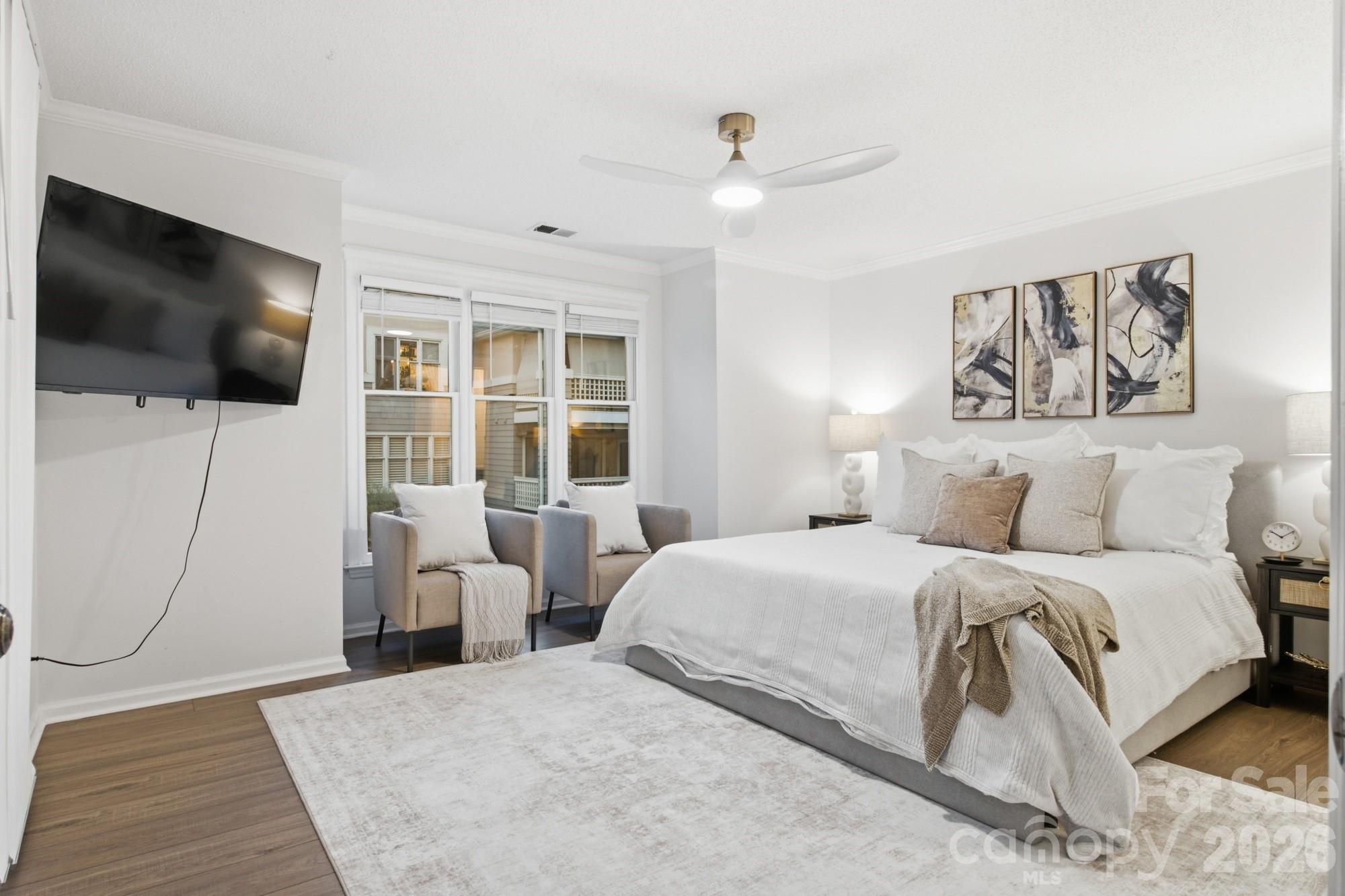 Furnished bedroom with a large white bed, abstract wall art, and two chairs beside the windows.