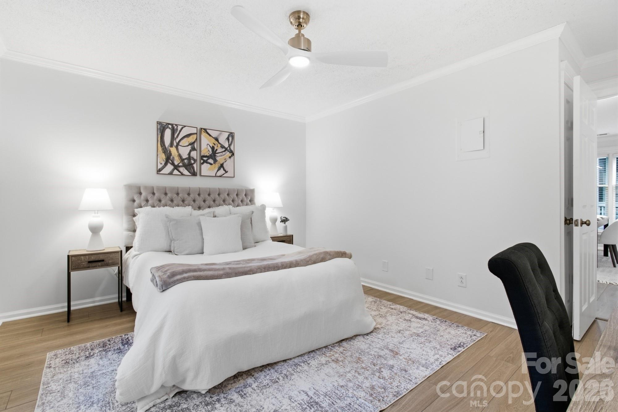 Staged bedroom with a white bed, tufted gray headboard, matching lamps, and abstract art.