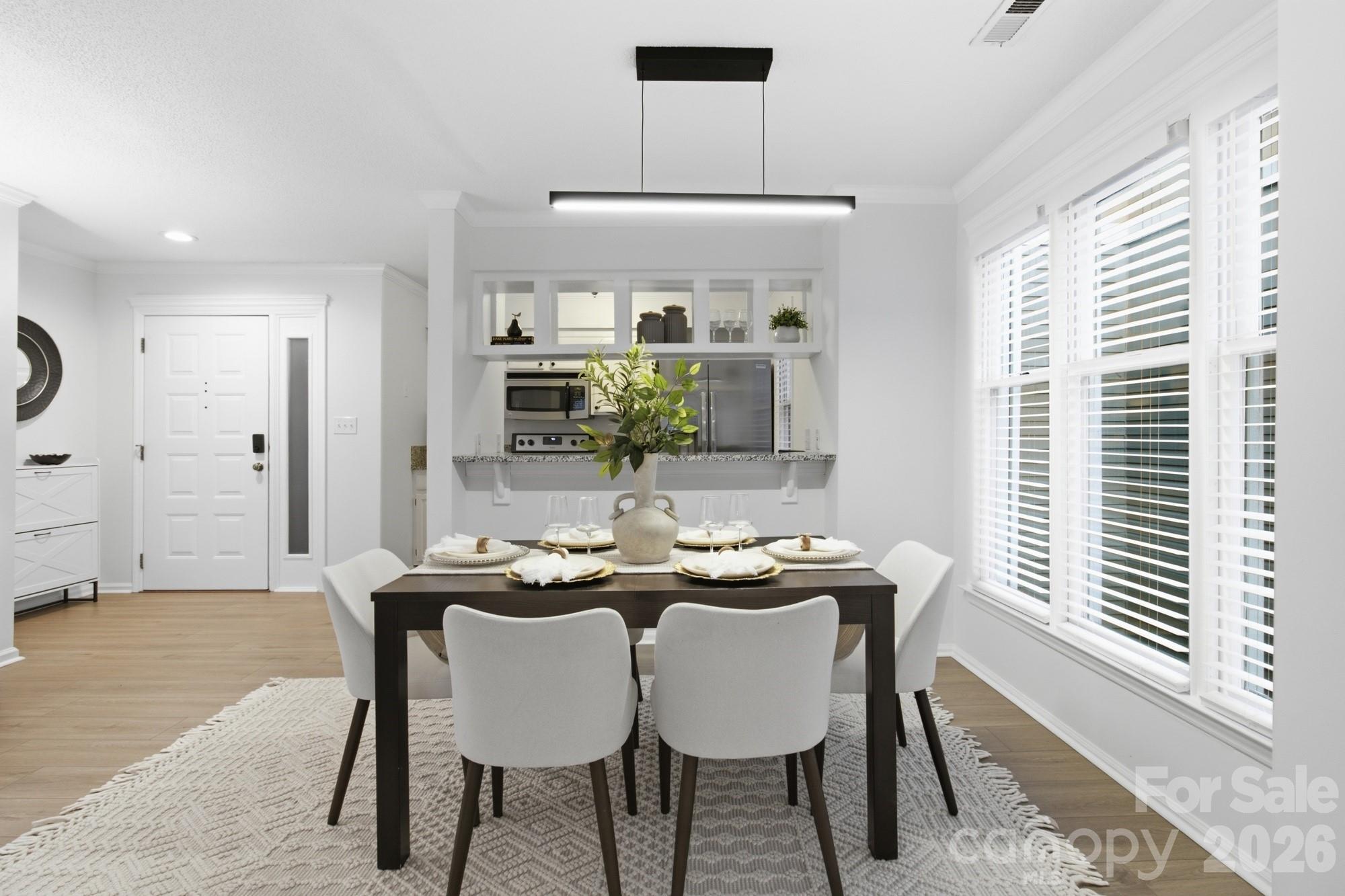 Staged dining room with a set table, white chairs, and a kitchen pass-through.