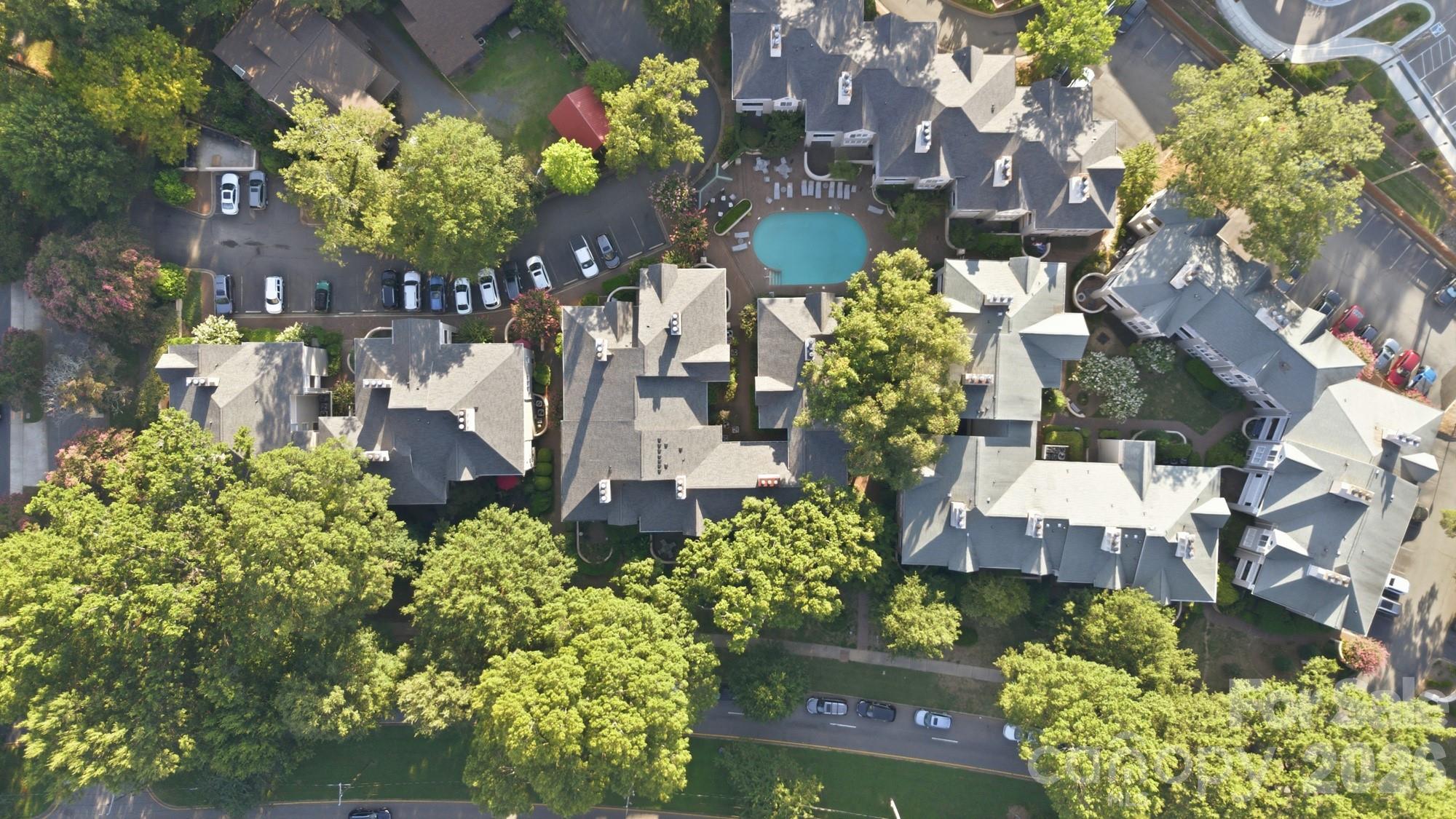 Aerial view of a tree-lined condominium complex with a central swimming pool and parking areas.