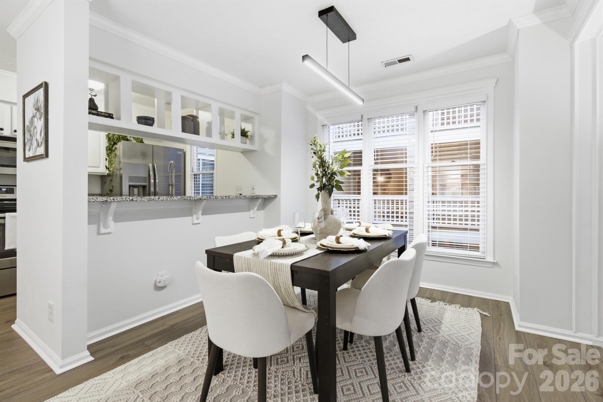 Bright dining area with a dark table, white chairs, and a kitchen pass-through.