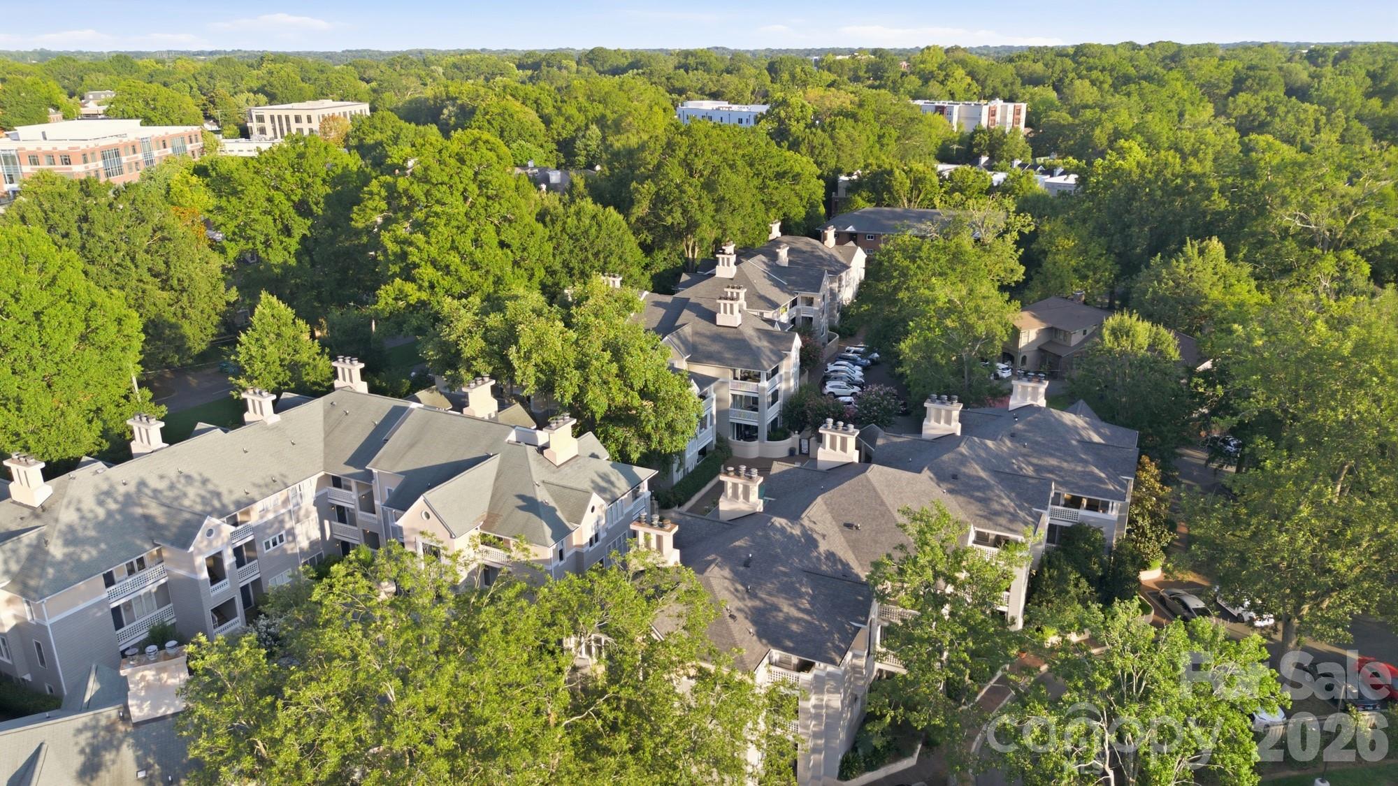 Aerial view of a tree-surrounded condominium complex with multiple buildings and parking areas.