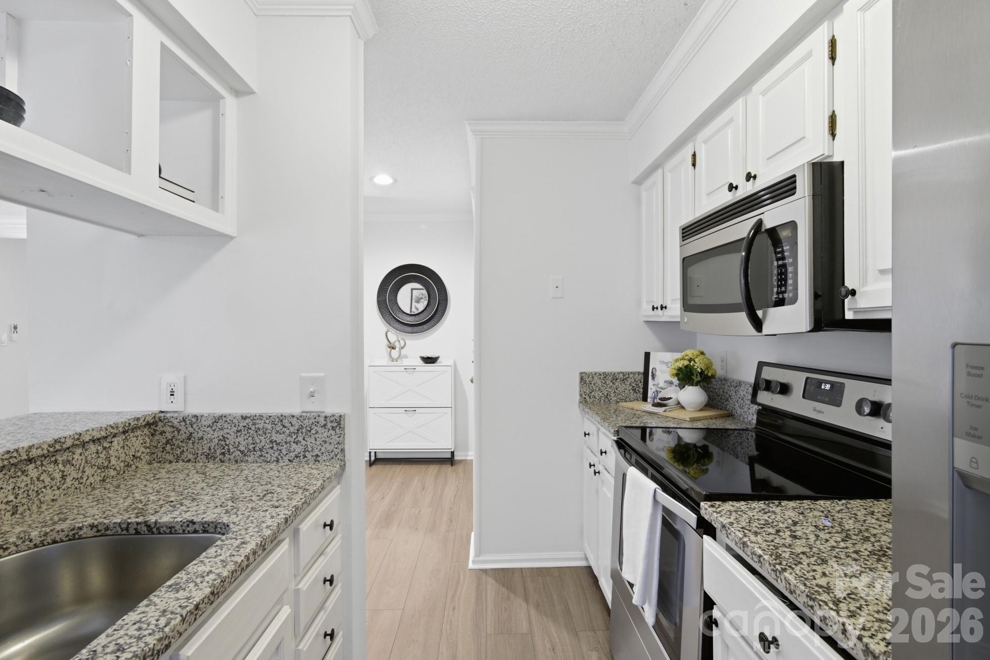 Kitchen with white cabinets, granite counters, stainless appliances, and light wood flooring.