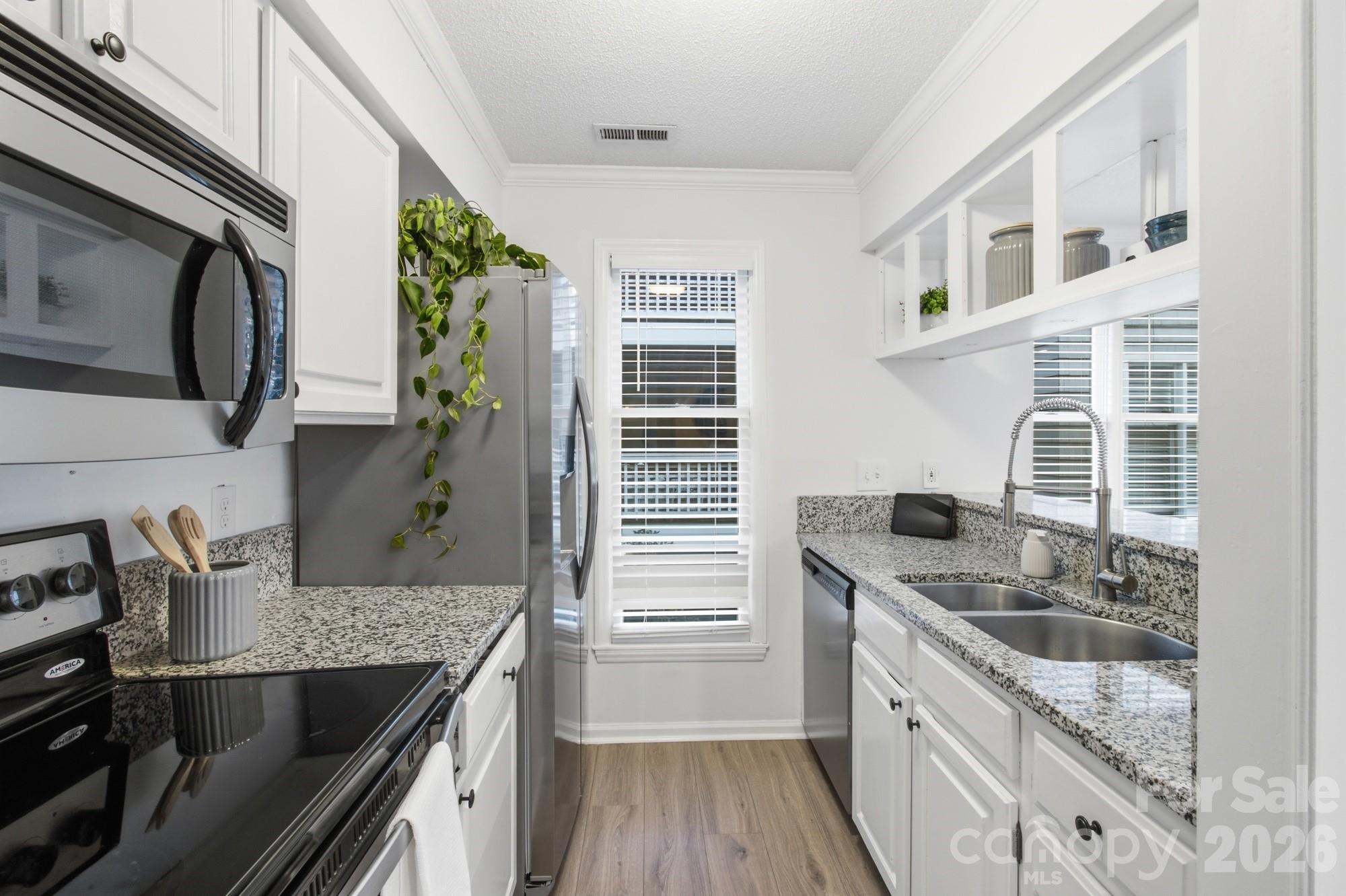 Galley kitchen with white cabinets, granite counters, stainless appliances, and a double-basin sink.