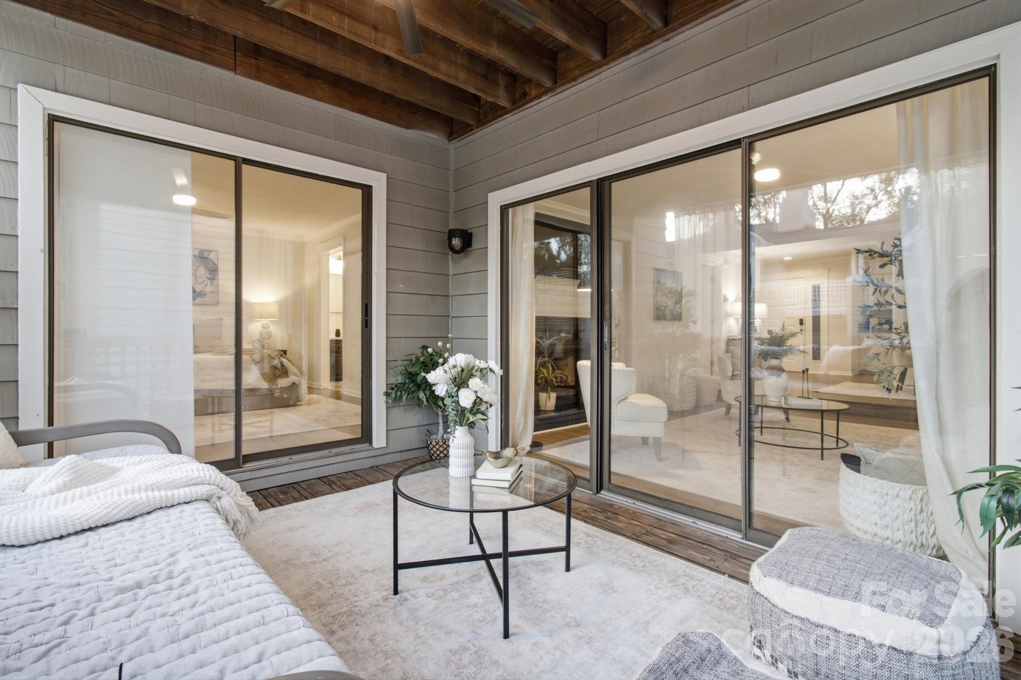 Covered patio with a wood ceiling, white seating, and sliding glass doors to the living room.