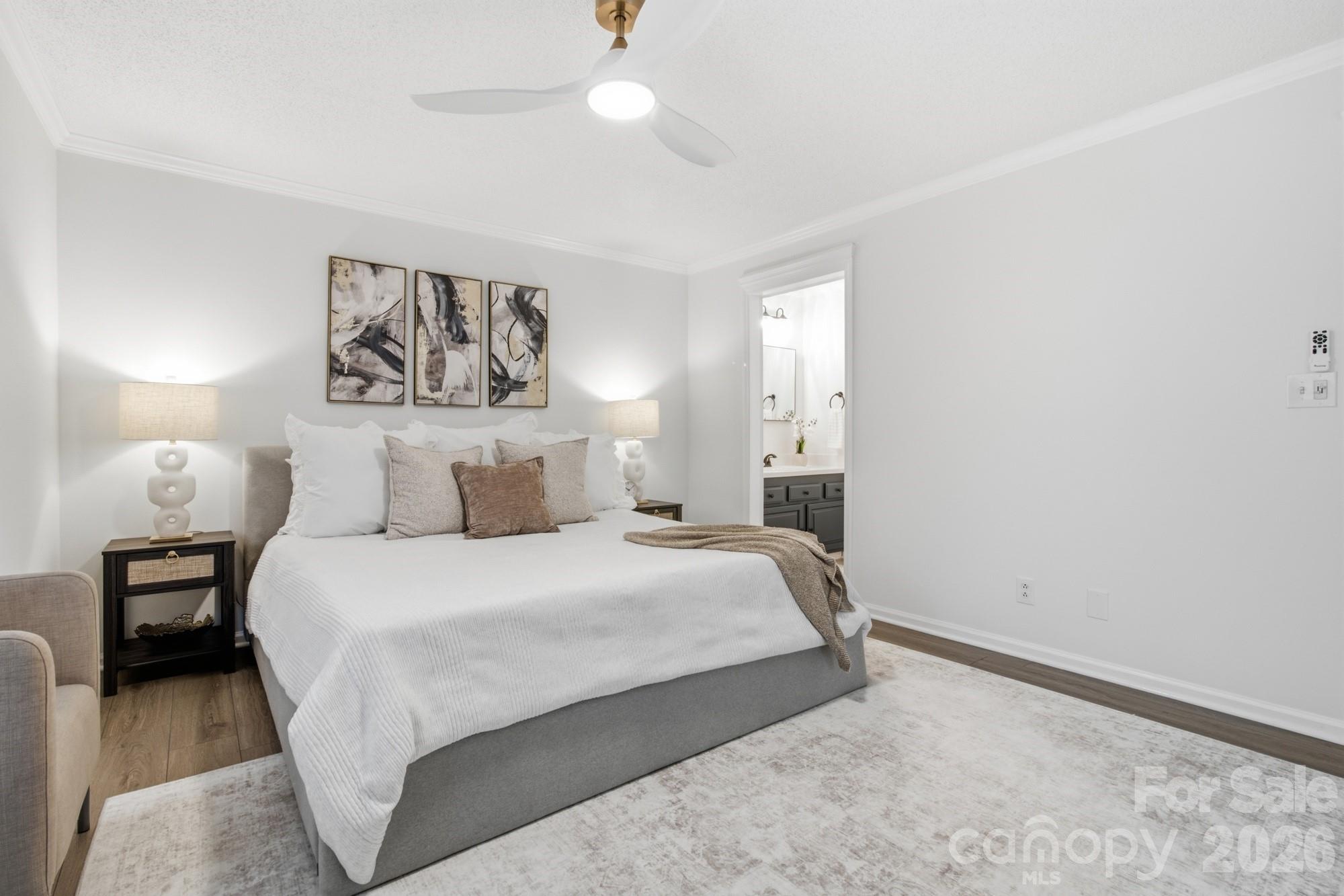 Furnished bedroom with a white bed, neutral pillows, abstract wall art, and an adjoining bathroom vanity.