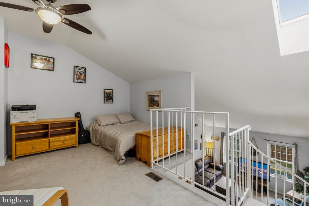 Loft bedroom with a sloped ceiling, beige bed, wooden furniture, and railing overlooking the lower level.