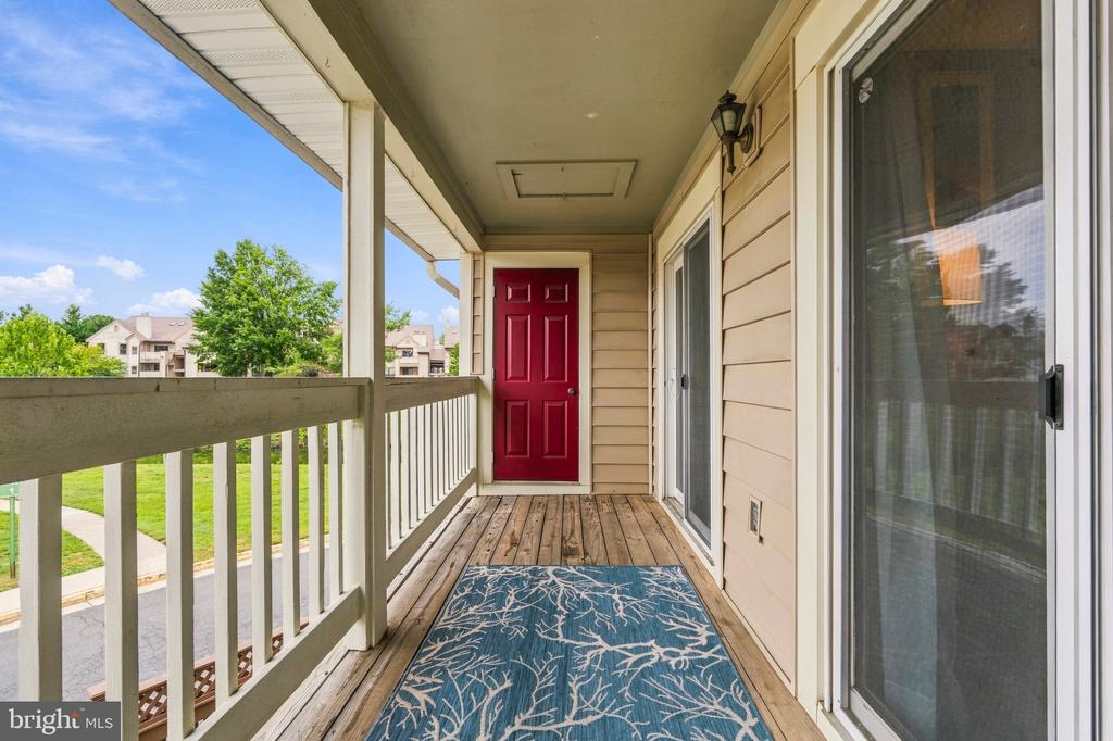 Covered apartment balcony with a red door, white railing, and blue patterned rug.