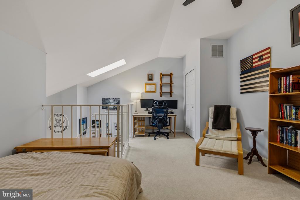 Furnished loft bedroom with a sloped ceiling, desk workspace, railing, and lounge chair.