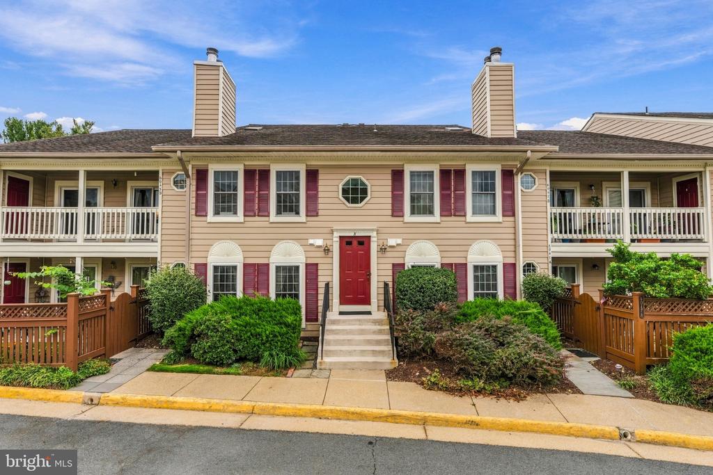 Two-story beige condominium exterior with burgundy shutters, balconies, fenced patios, and a central entrance stairway.
