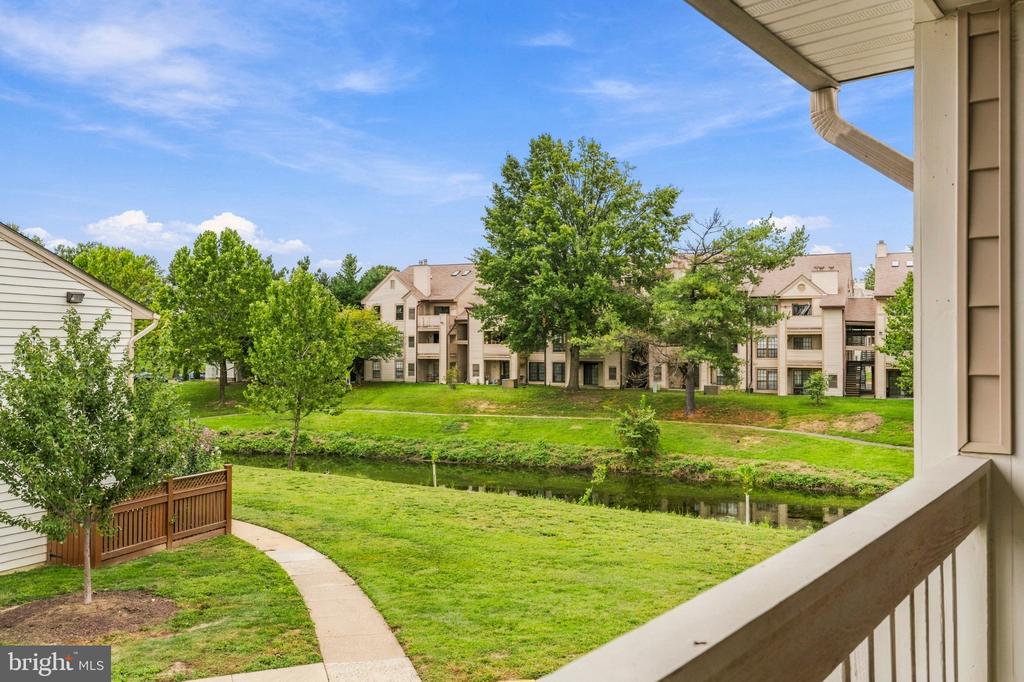 Balcony view across a landscaped lawn and pond toward neighboring apartment buildings and mature trees.