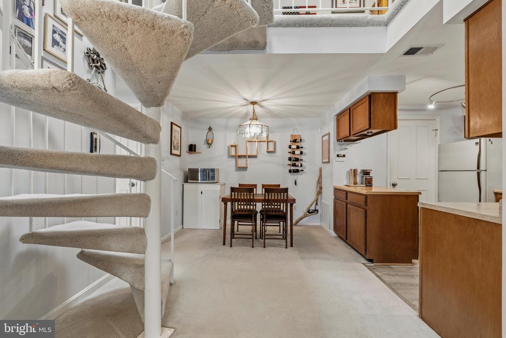 Dining area and kitchen with wood cabinetry, a carpeted spiral staircase, and an upper-level loft.