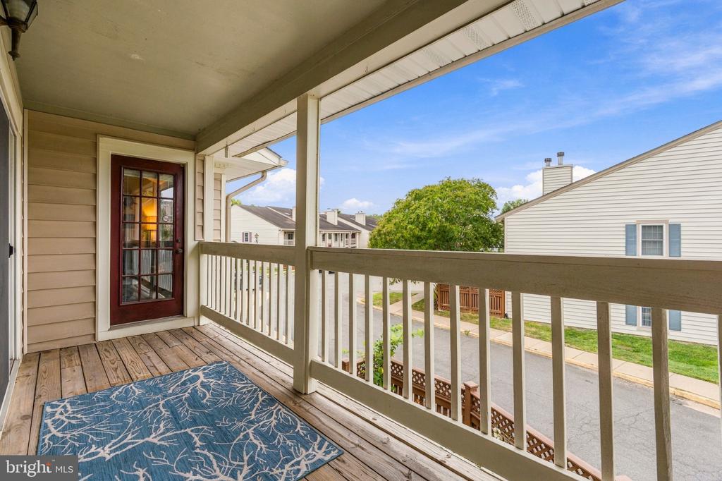 Covered wooden balcony with a blue patterned rug overlooking neighboring townhouses.