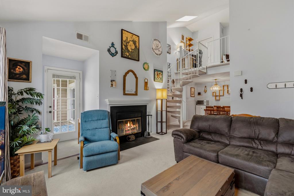 Living room with a lit fireplace, blue armchair, and spiral staircase to an upper-level loft.