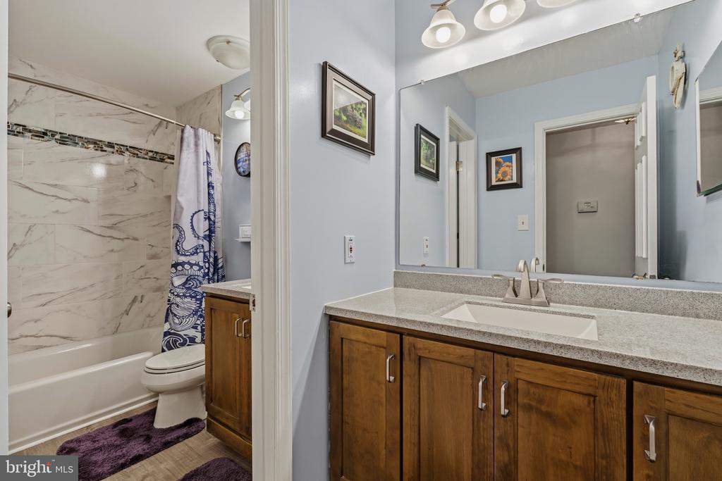 Bathroom with wood vanity and large mirror beside a tub with marble-patterned tile.