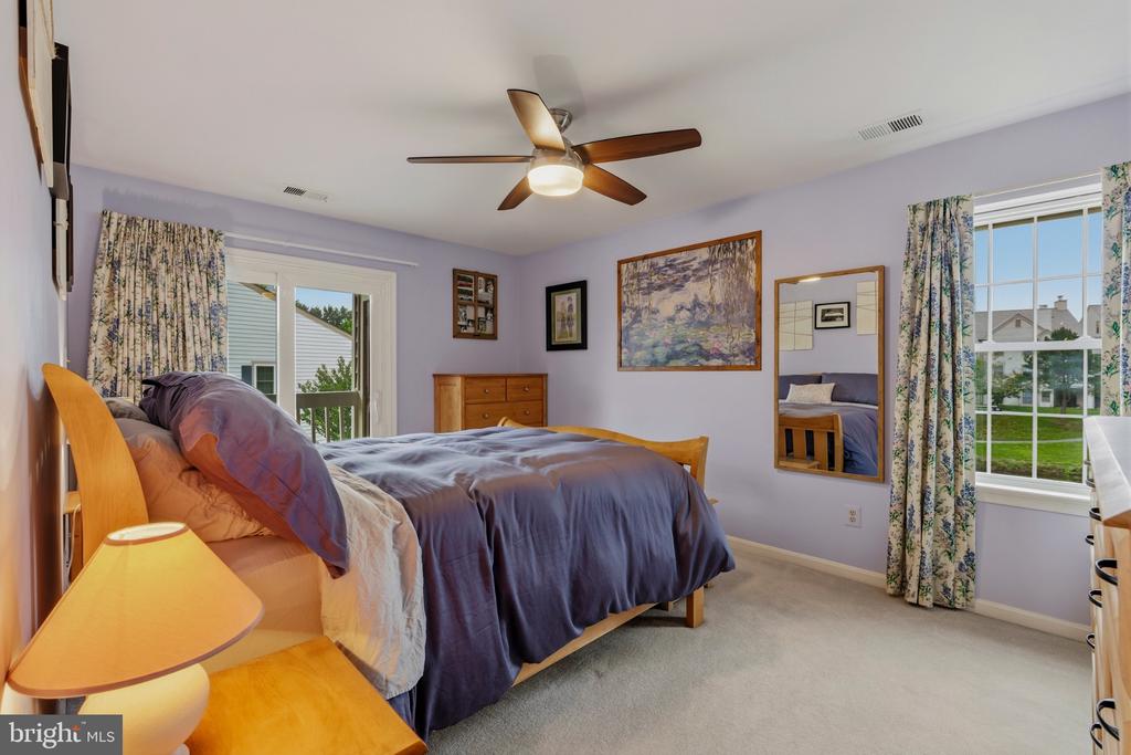 Bedroom with purple bedding, lavender walls, and large windows overlooking neighboring homes.