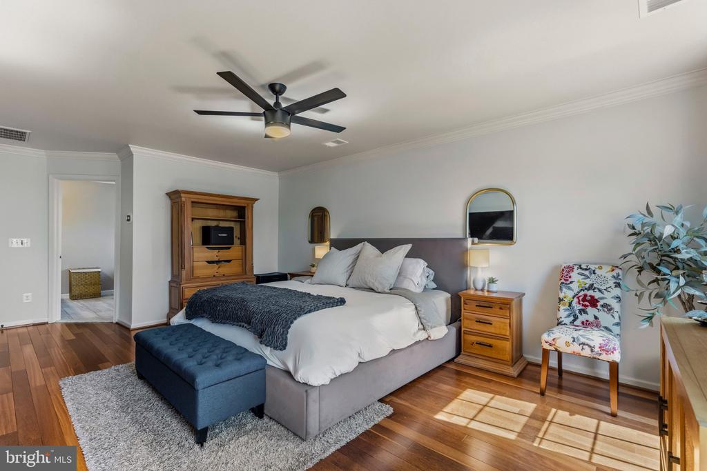Furnished bedroom with a gray upholstered bed, dark wood floors, and a floral accent chair.