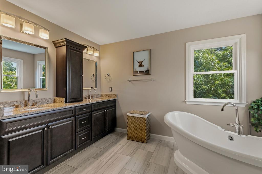 Bathroom with a double vanity, freestanding tub, and window overlooking greenery.