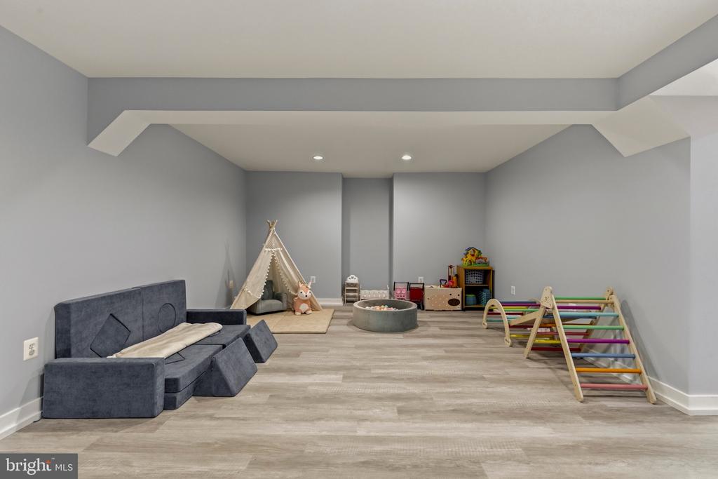 Playroom with a gray sofa, teepee, toys, and colorful climbing frame.