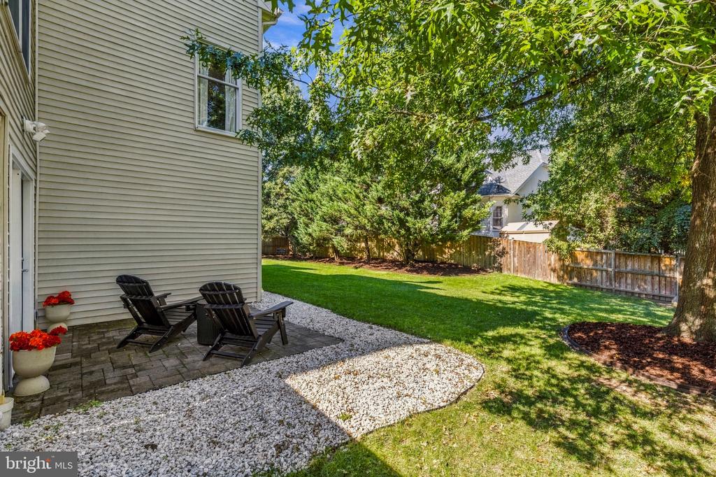 Backyard patio with two Adirondack chairs, gravel landscaping, fenced lawn, and mature shade trees.