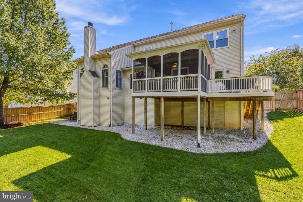 Rear of a two-story home with a raised screened porch, deck, and broad lawn.