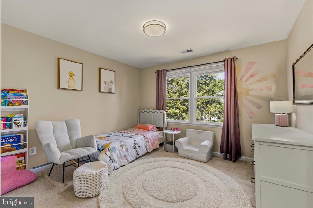 Bright child's bedroom with a single bed, reading chairs, and a large window overlooking trees.