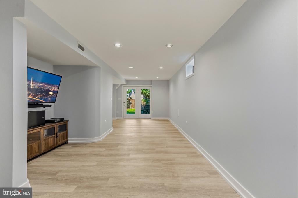 Long finished living area with light wood flooring, a TV console, and glass doors to the yard.