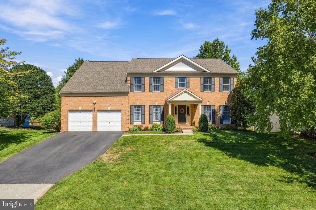 Two-story brick house with twin garage doors, front porch, and broad green lawn.
