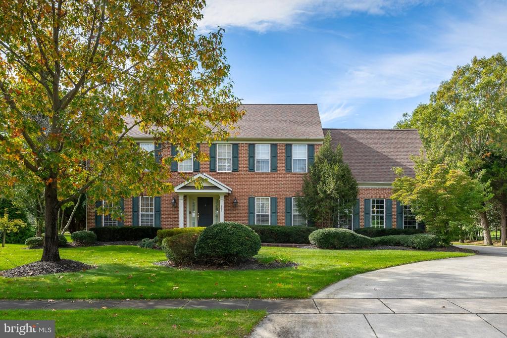 Two-story brick house with dark shutters, a covered entrance, and mature autumn trees.