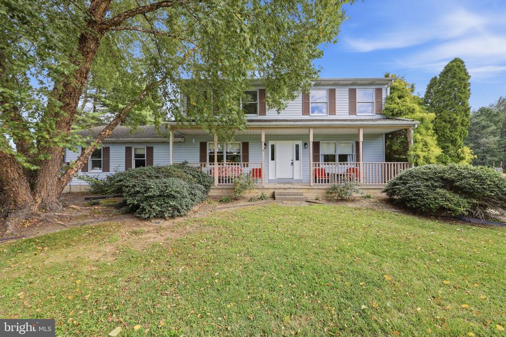 Two-story house with a long covered porch, mature trees, and a broad lawn.
