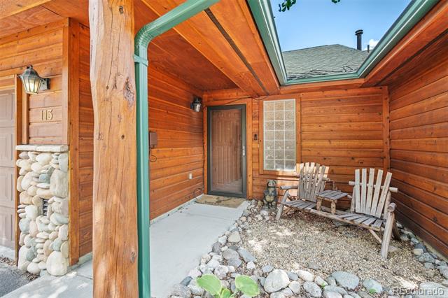 Covered log entry porch with a skylight, two Adirondack chairs, and a stone-and-gravel bed.