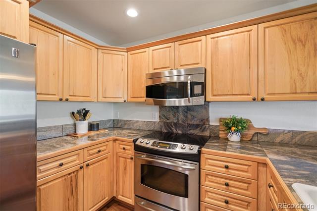Kitchen with honey-toned cabinets, dark stone counters, and stainless steel appliances.