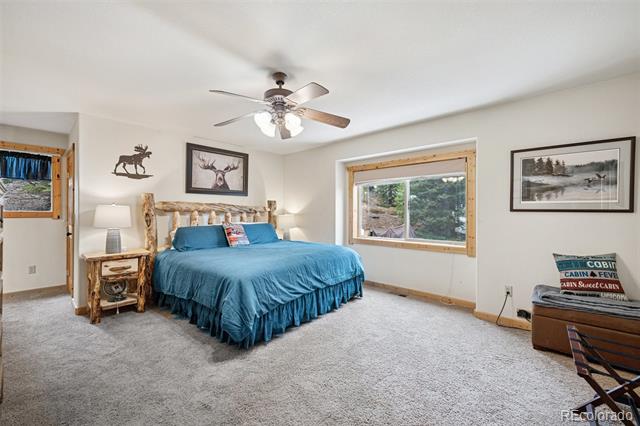 Bedroom with a blue bedspread, rustic log headboard, wood-trimmed windows, and a ceiling fan.