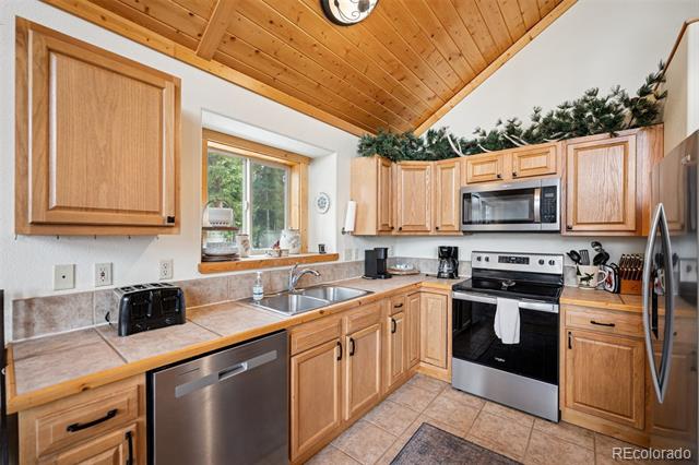 Kitchen with light wood cabinetry, stainless steel appliances, and a vaulted wood ceiling.