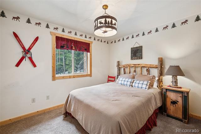 Rustic bedroom with a log bed, plaid pillows, crossed red skis, and a tree-lined view through the window.