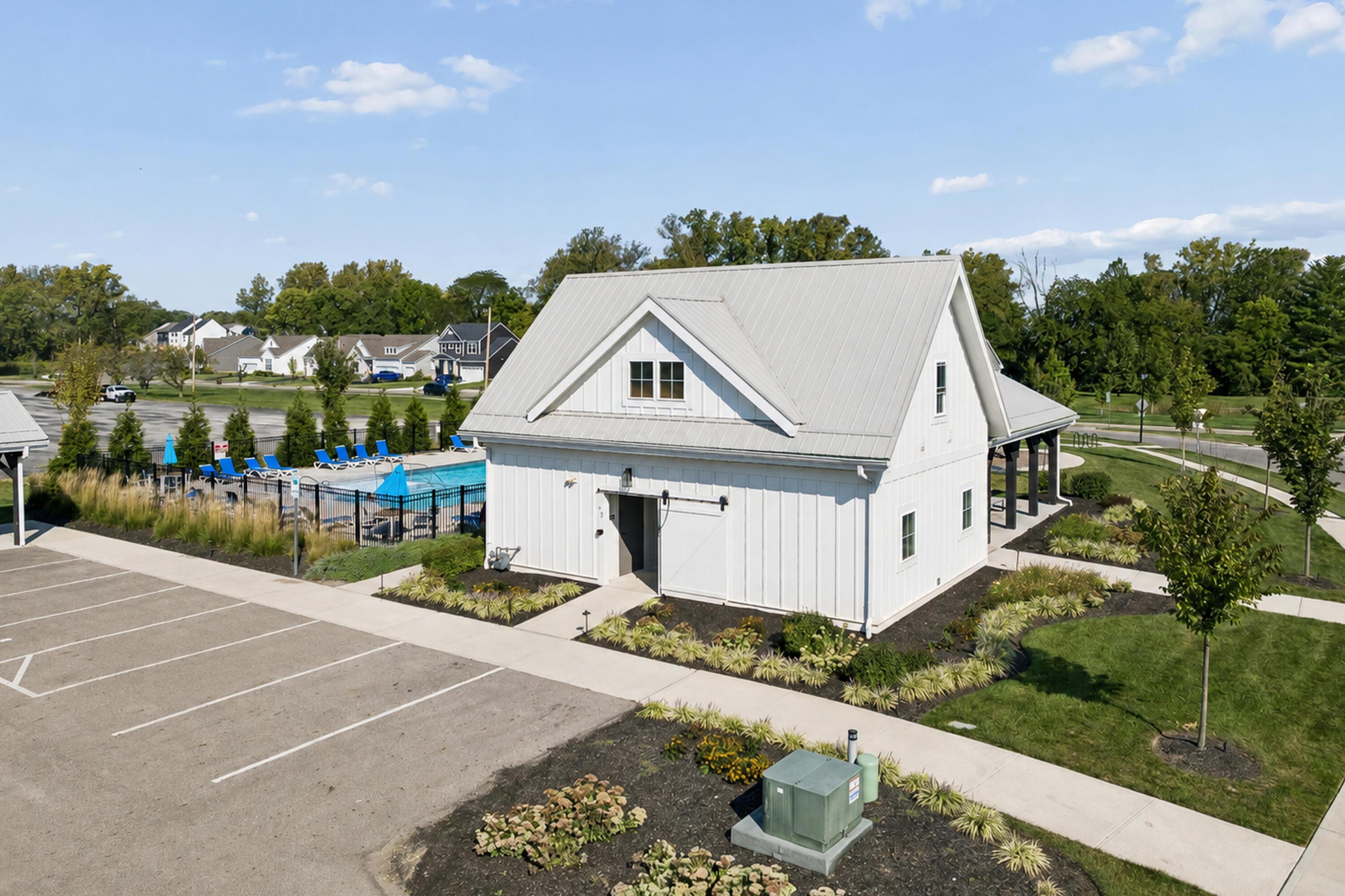 White community clubhouse beside a fenced outdoor pool and landscaped parking area.