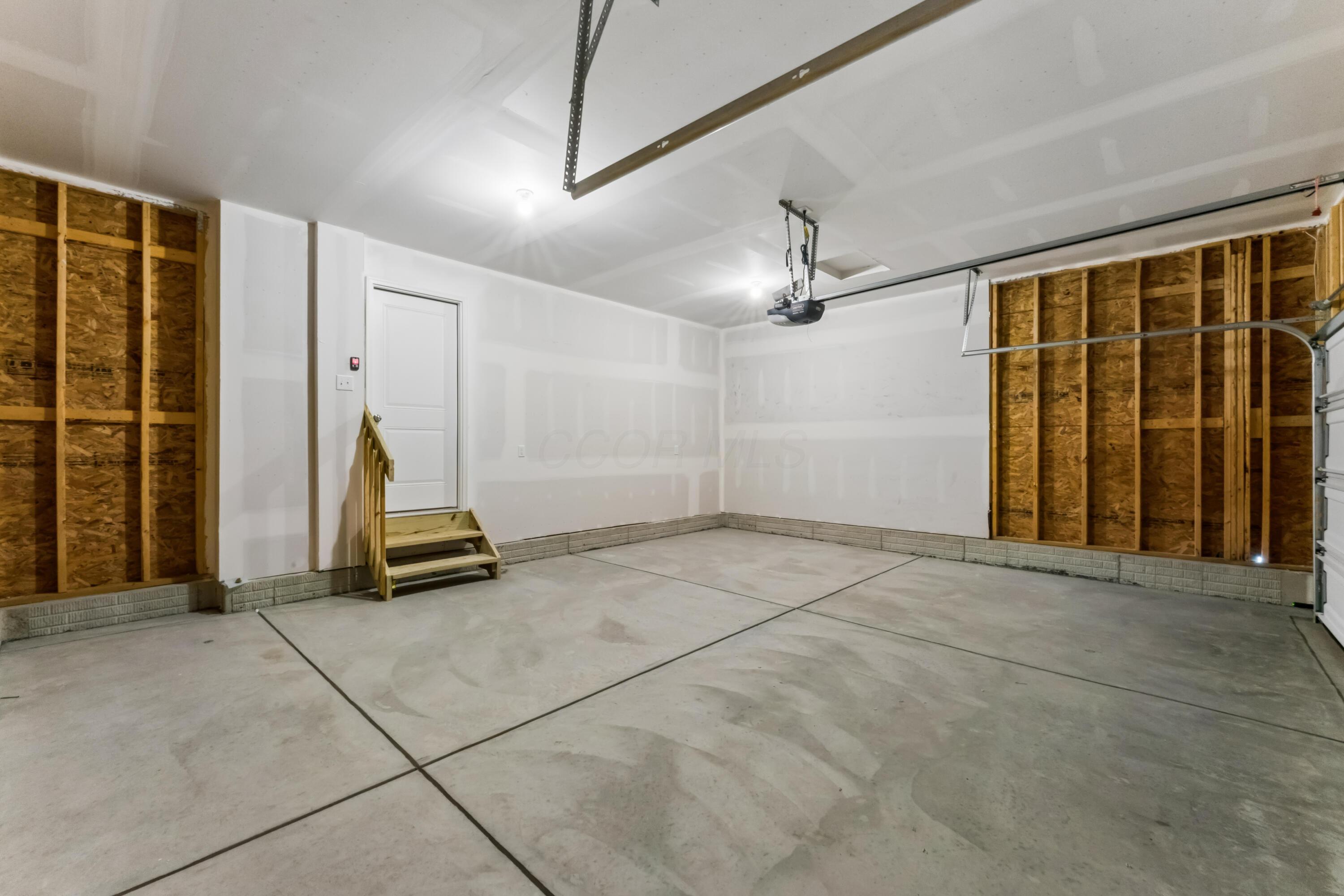 Unfinished garage with exposed wall framing, concrete floor, and steps to a side door.