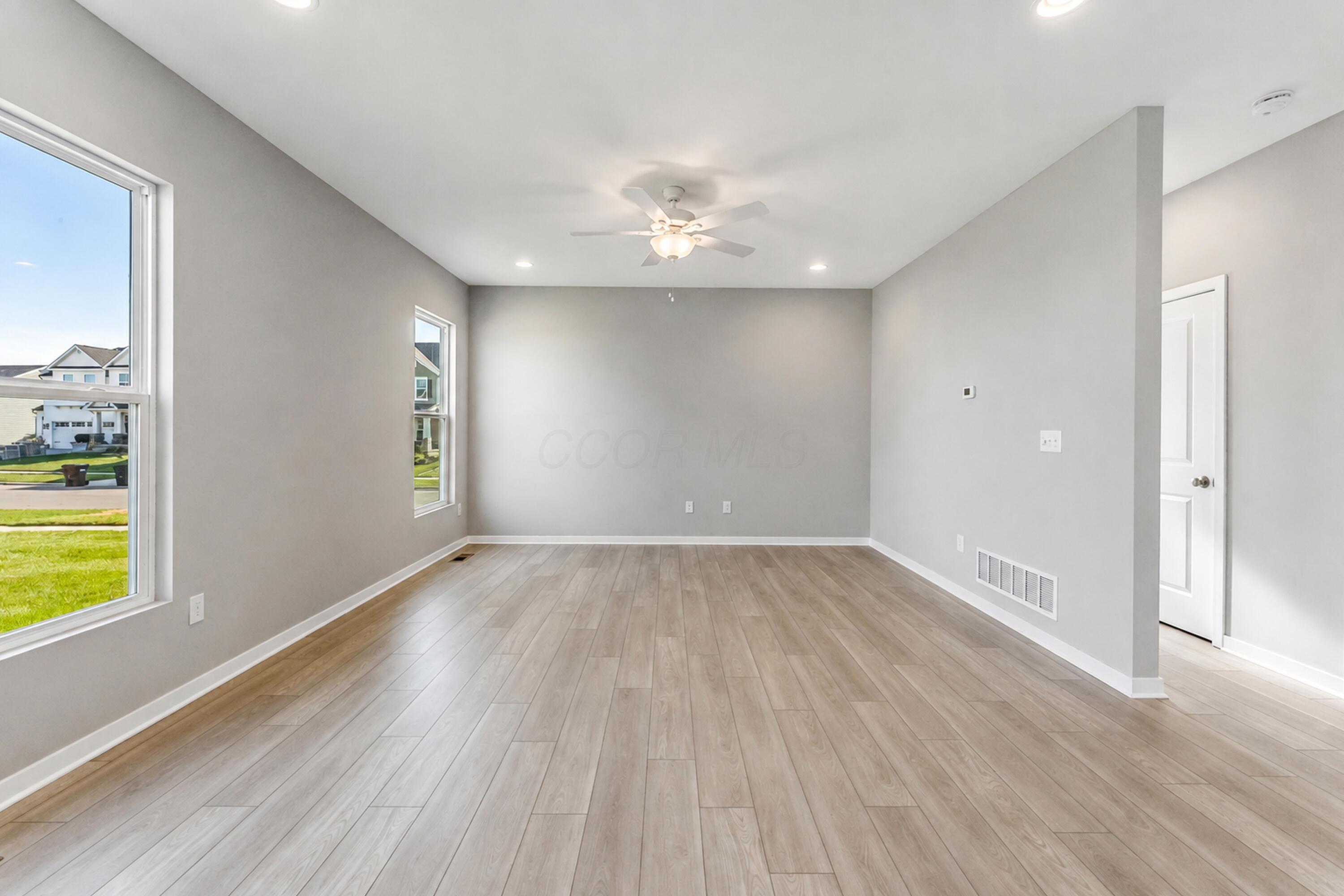 Vacant room with light plank flooring, gray walls, two windows, and a ceiling fan.