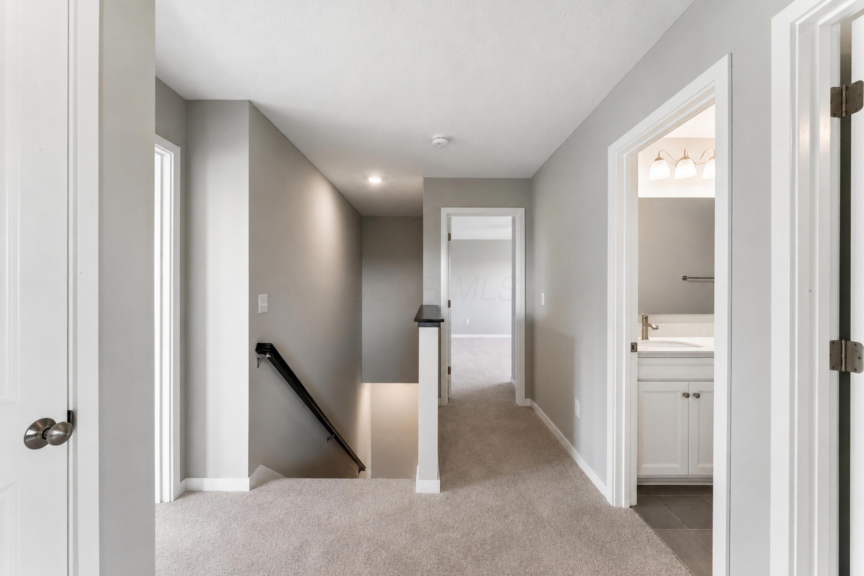 Upstairs hallway with beige carpet, a stairwell, and a bathroom doorway.