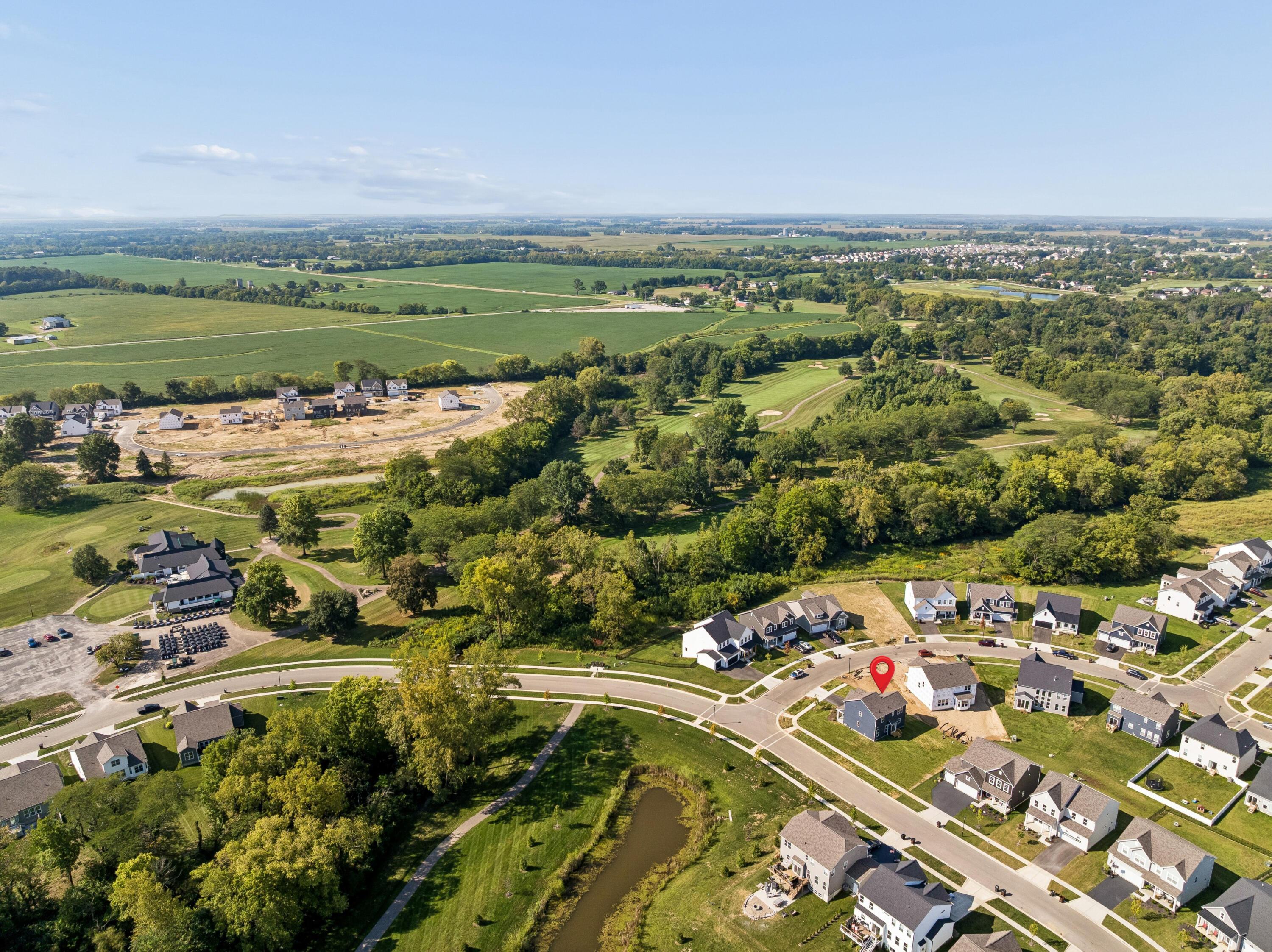 Aerial neighborhood view with a red marker over a home beside a golf course and wooded creek.