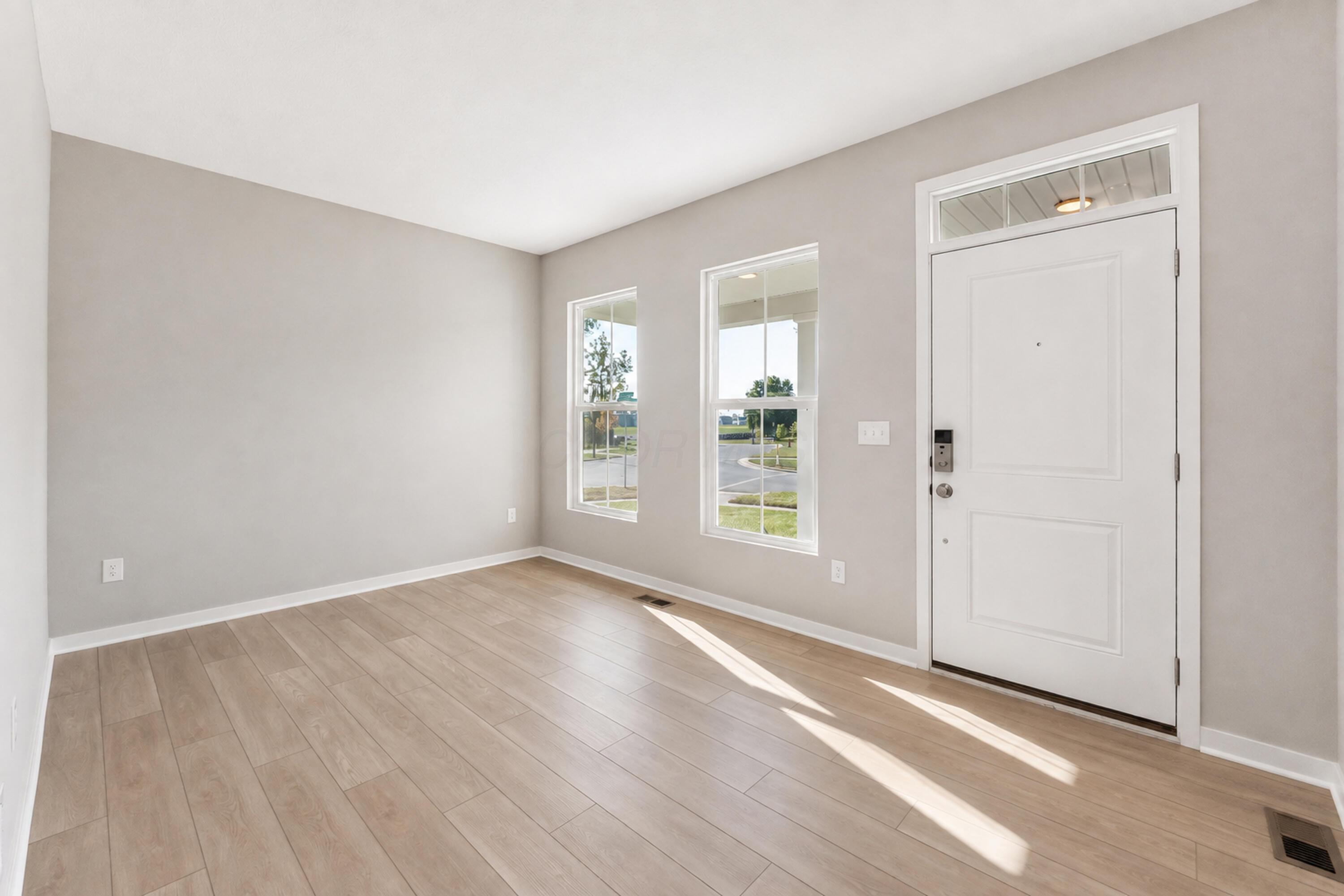 Vacant entry foyer with light plank flooring, two tall windows, and a white front door.