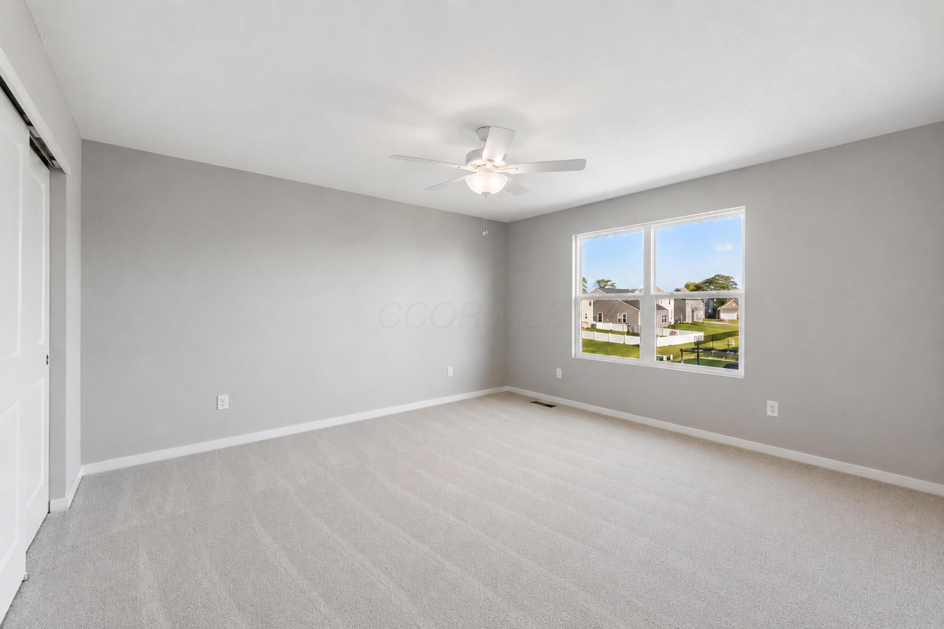 Empty bedroom with gray walls, light carpet, a ceiling fan, and a large window.
