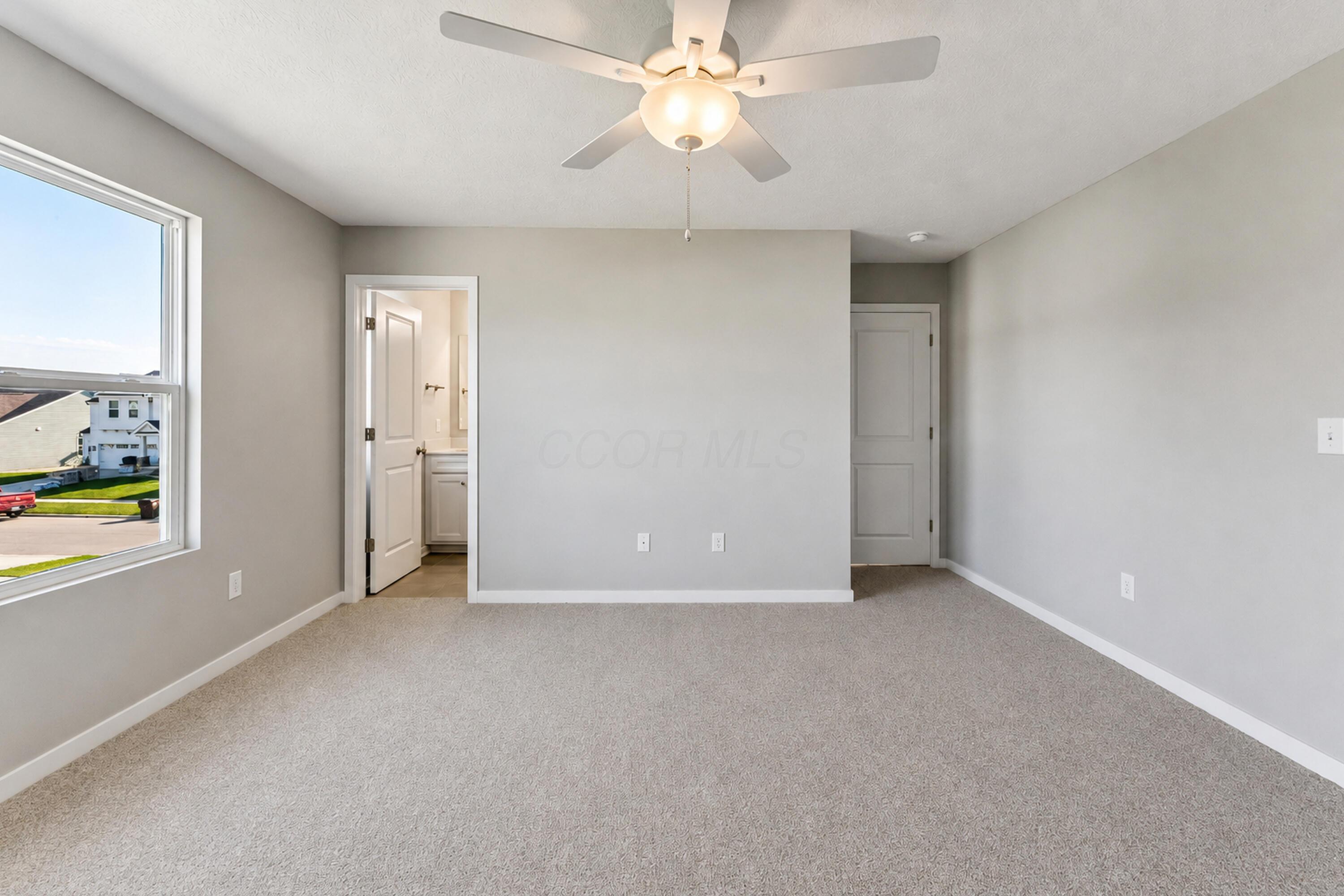 Vacant bedroom with beige carpet, a ceiling fan, and a large window.
