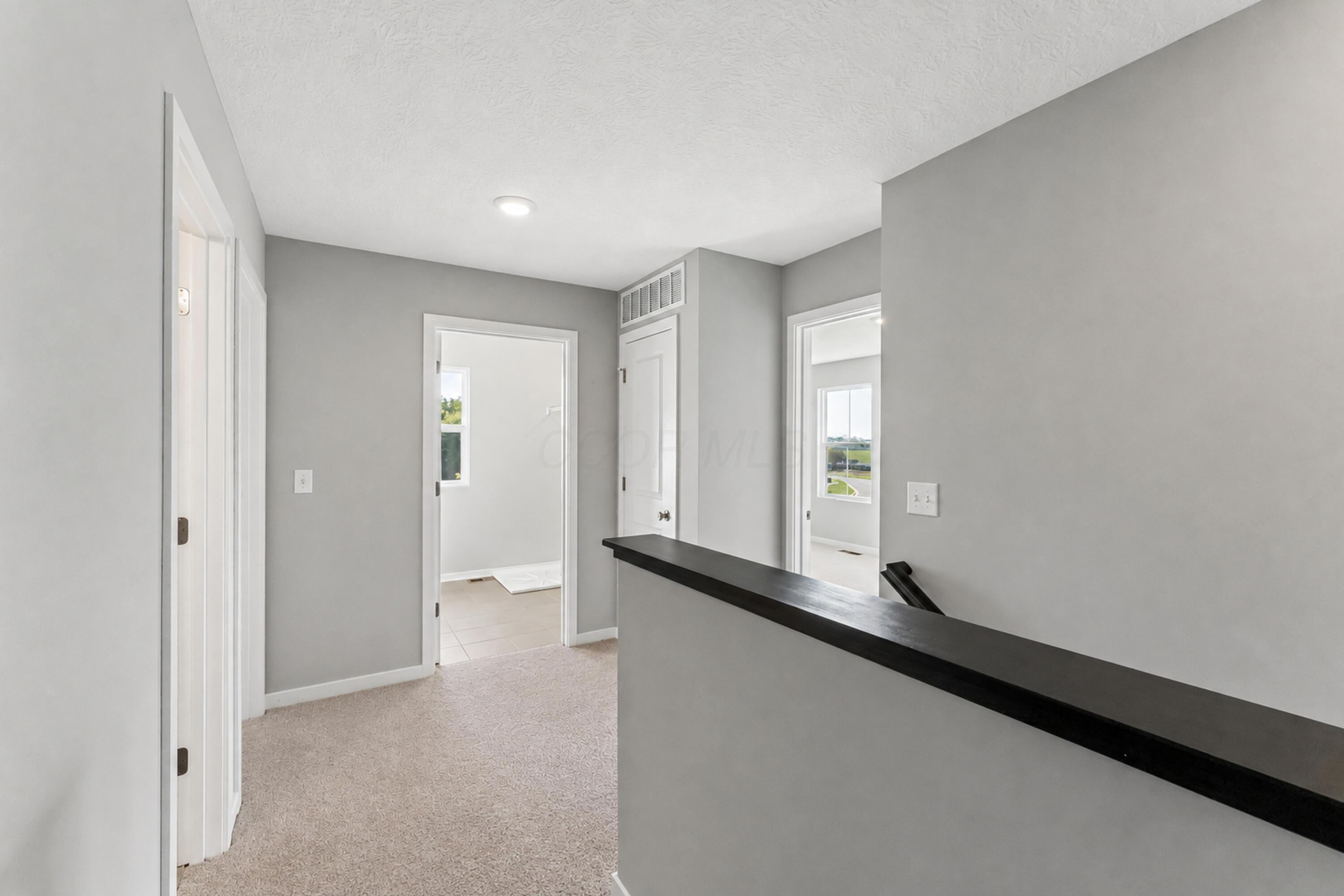 Carpeted upstairs hallway with gray walls, a black stair railing, and open doorways.