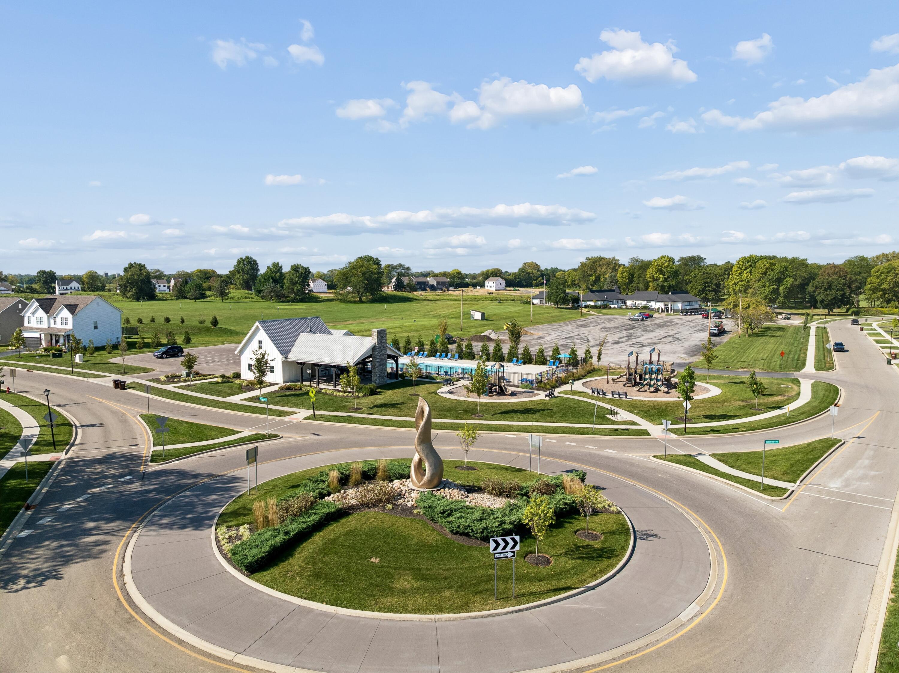 Aerial view of a residential community with a pool, playground, and landscaped roundabout.