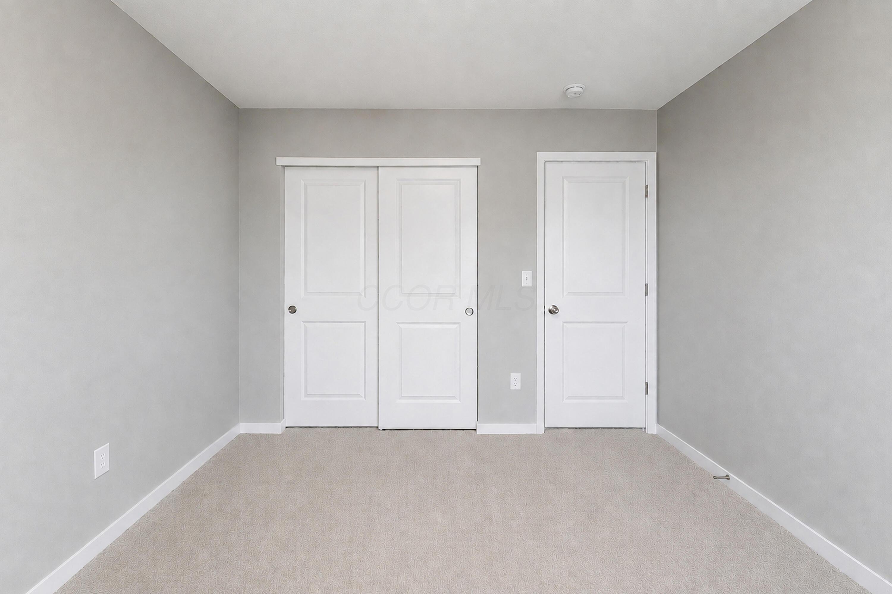 Empty carpeted room with gray walls, white sliding closet doors, and a separate hinged door.