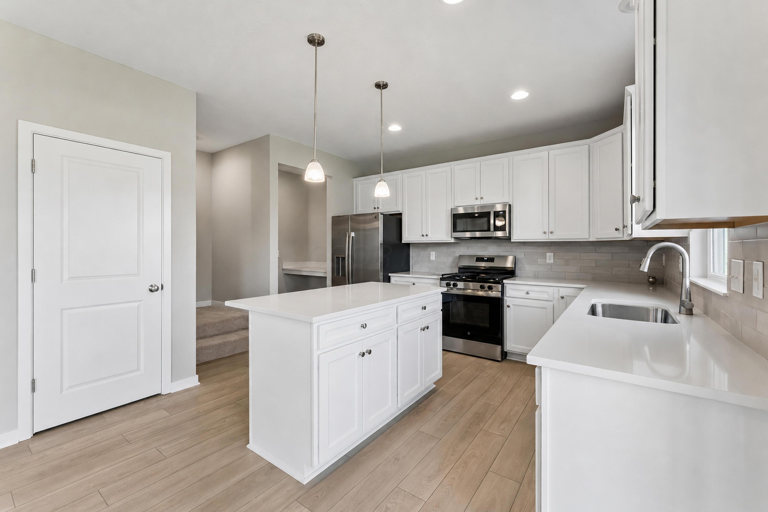 Modern kitchen with a white island, stainless steel appliances, and gray tile backsplash.