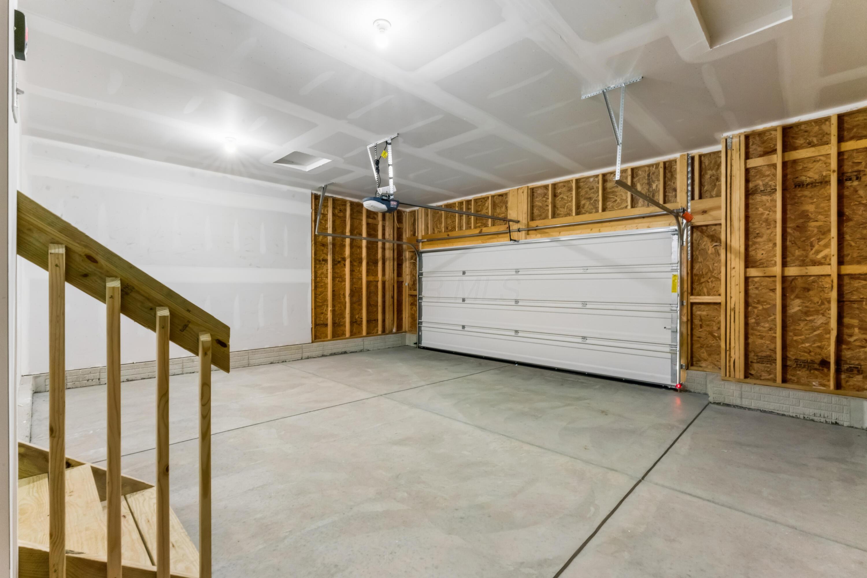 Unfinished garage with exposed wall framing, a closed overhead door, and wooden stairs.